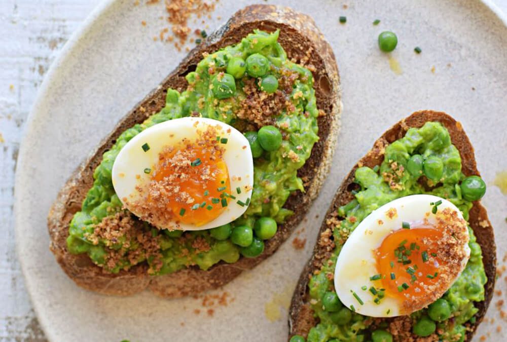 TOSTADAS CON PURÉ DE ARVEJAS Y PALTA, HUEVOS SOFT Y POLVO DE TOCINO